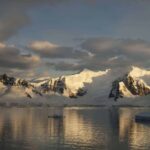 Dusk and flat calm water off the shore of a mountain landscape in Antarctica.